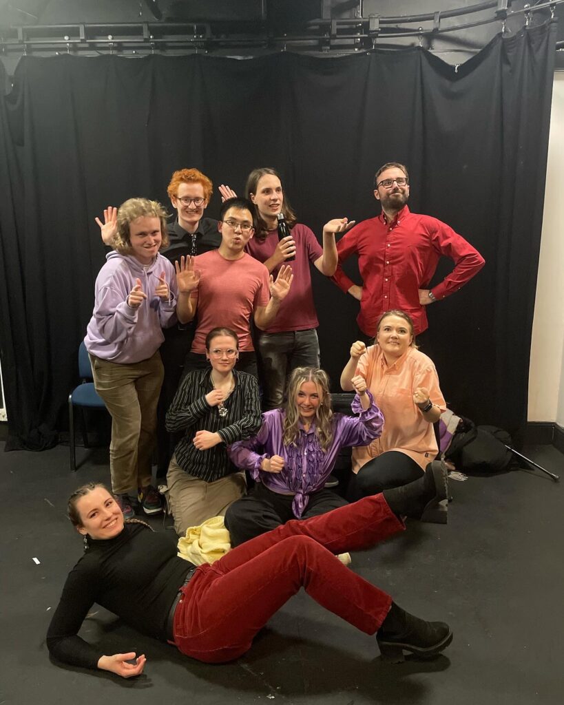 A group of people doing improv in character and looking proud of themselves after a successful show